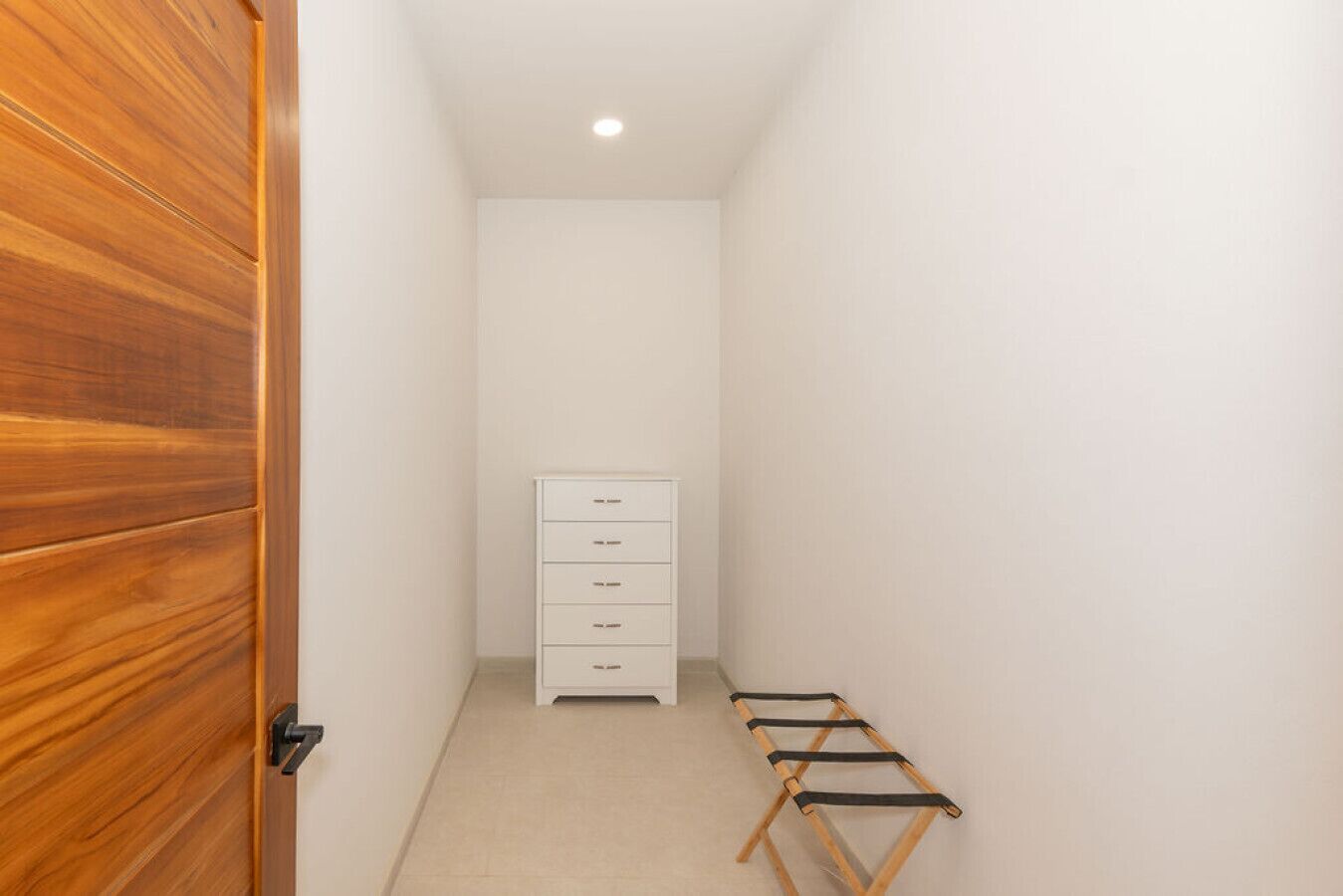 A narrow hallway with a wooden door, a white dresser, and a drying rack.