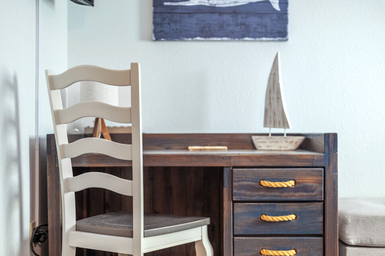 Una sedia di legno con schienale a listelli e una scrivania con cassetti e una piccola nave in miniatura.