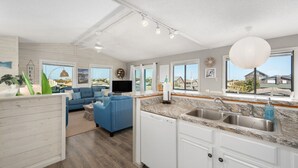 Uma cozinha moderna com máquina de lavar louça embutida, uma janela grande com vista e um sofá azul na sala de estar.