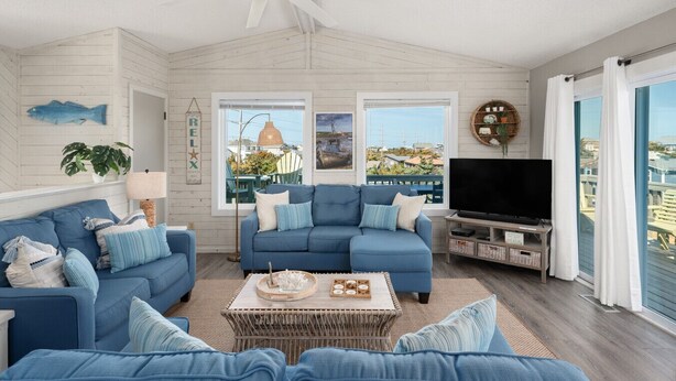 Sala de estar com sofá azul, televisão de tela plana e ampla janela com vista para o mar.