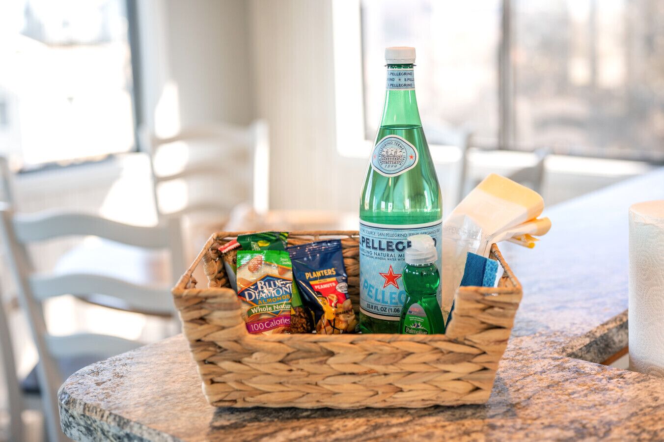 A wicker basket containing snacks, a bottle of Pellegrino water, and a bar of soap on a marble countertop.