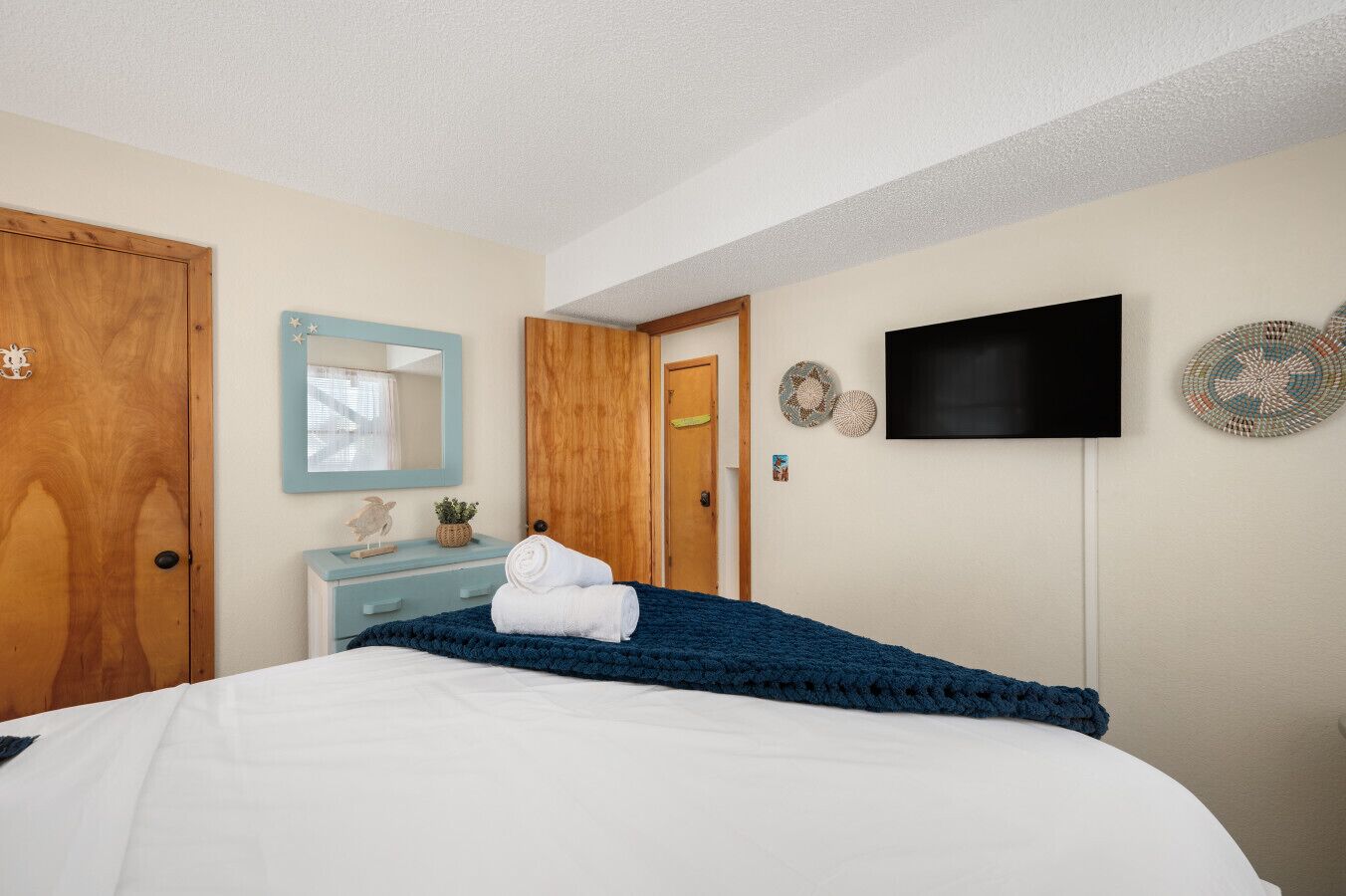 Une chambre à coucher avec un lit, une commode, un téléviseur et une porte.