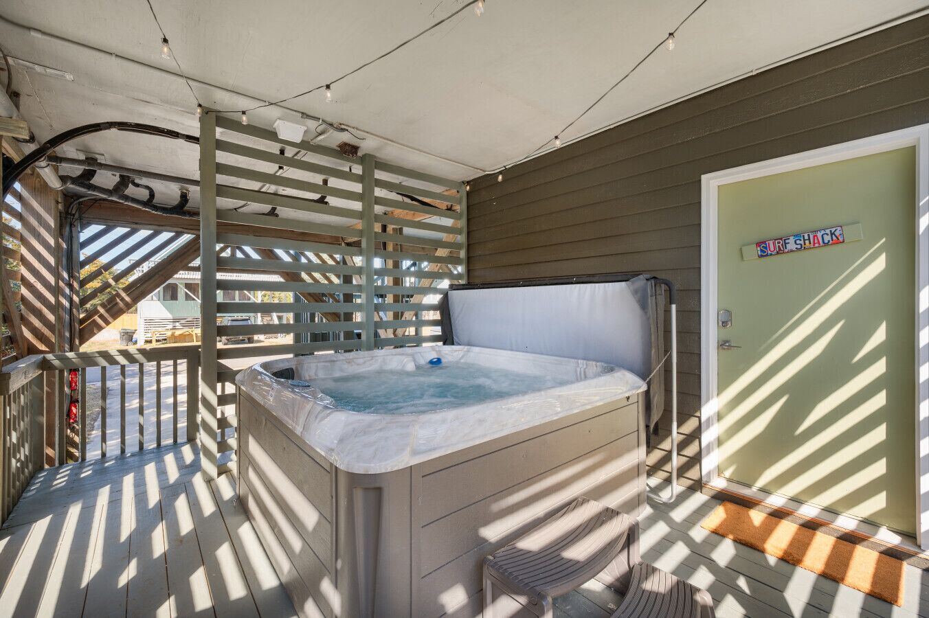A hot tub on a wooden deck with a door labeled 'SURF SHACK' and a metal railing.