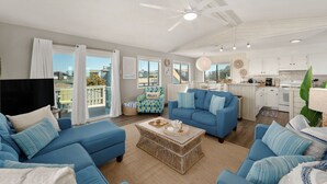 Uma sala de estar espaçosa, com um sofá azul, uma mesa de centro de vime e um ventilador de teto.