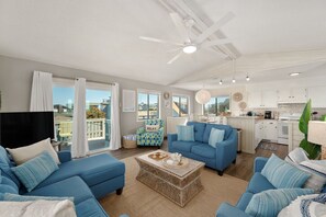 A spacious living room with a blue sofa set, a wicker coffee table, and a ceiling fan. - King Tide Rising by Rather Be Properties (Avon)
