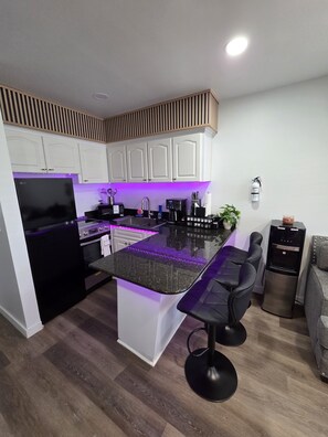 A modern kitchen with white cabinets, a black refrigerator, a built-in oven, a coffee maker, and a water dispenser.