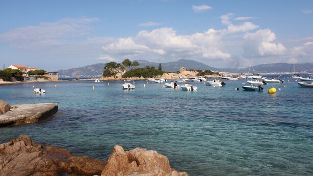 Zona costera con barcos, costa rocosa y montañas al fondo.