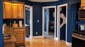 A kitchen with wooden cabinets, a countertop, and a stove. There is a doorway leading to a living area with a patterned rug. - 3-Bedroom house in tree-lined neighborhood in Millcreek (Salt Lake City)