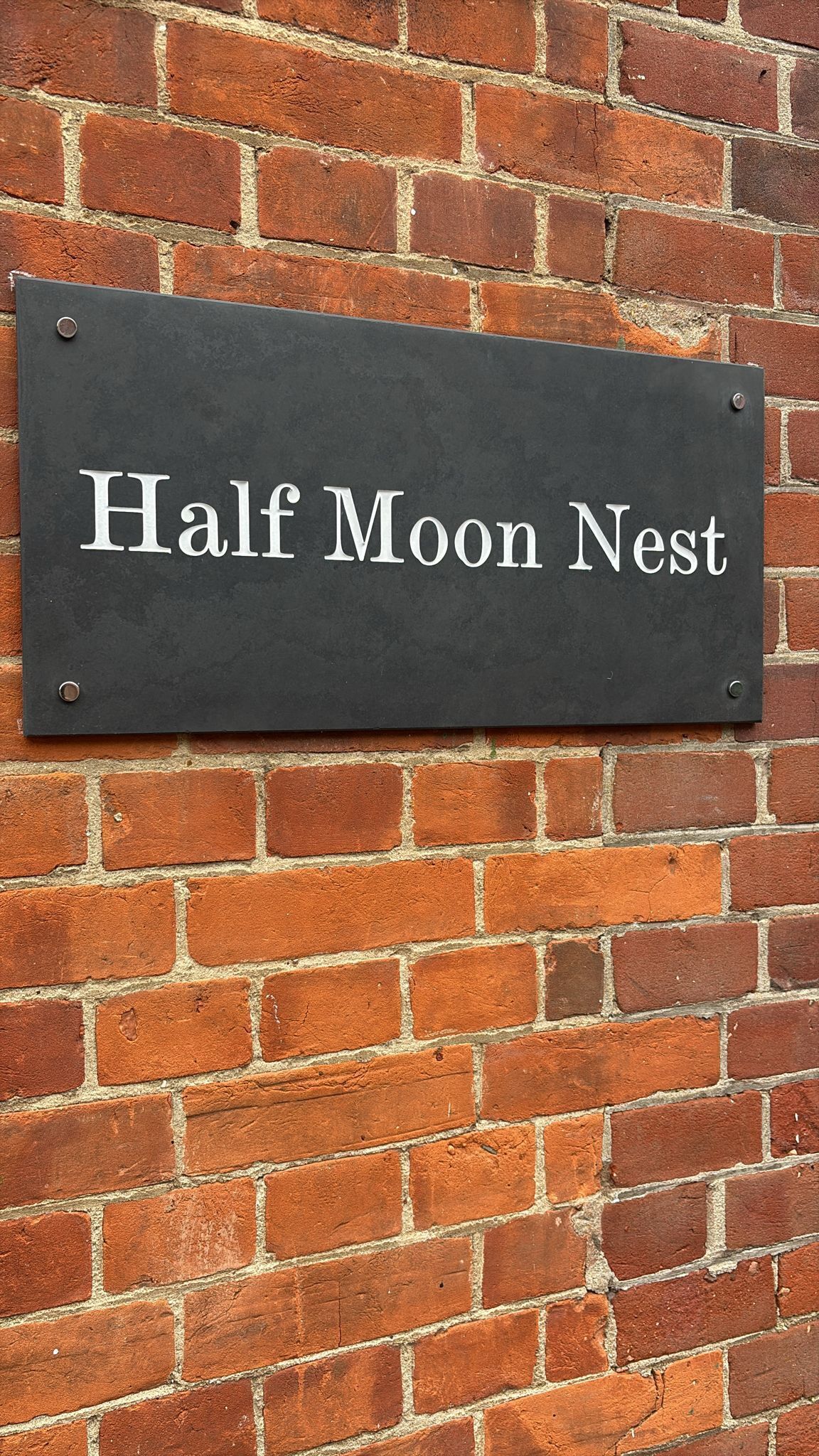 Een bord aan een bakstenen muur met de tekst 'Half Moon Nest'.