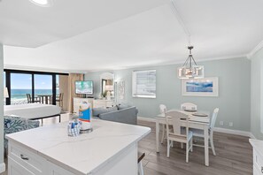 A modern living room with a large window, a dining area, and a kitchen with a marble island. - Beachside II #4247 (Miramar Beach)