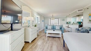 A modern bedroom with a bed, a white dresser, a sofa, a coffee table, and a kitchen area in the background. - Beachside II #4247 (Miramar Beach)