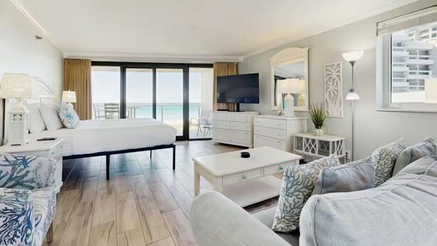 A hotel room with a bed, a sofa, a TV, a desk, and a view of the ocean. - Beachside II #4247 (Miramar Beach)