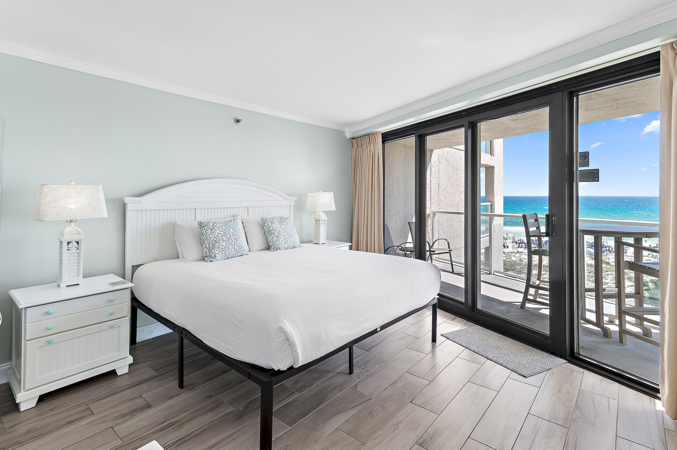 A bedroom with a bed, nightstands, and a view of the ocean.