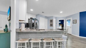 A modern kitchen with a central island, bar stools, and a dining area. - Sunnyside Up in PCB (Panama City Beach)