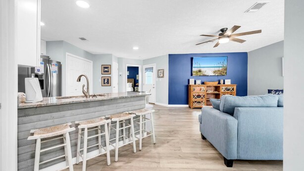 A modern kitchen with a bar area, a blue accent wall, and a ceiling fan. - Sunnyside Up in PCB (Panama City Beach)