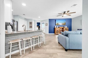 A modern kitchen with a bar area, a blue accent wall, and a ceiling fan. - Sunnyside Up in PCB (Panama City Beach)