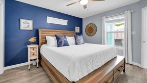 A bedroom with a wooden bed, a nightstand, a ceiling fan, and a window with curtains. - Sunnyside Up in PCB (Panama City Beach)