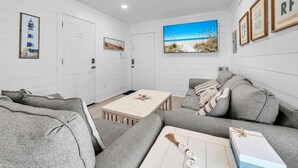A modern living room with a sofa, a coffee table, and a painting of a beach scene. - Sunnyside Up in PCB (Panama City Beach)