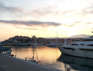 Eine Marina mit vertäuten Booten, eine Uferpromenade und eine Stadtansicht mit Gebäuden im Hintergrund.