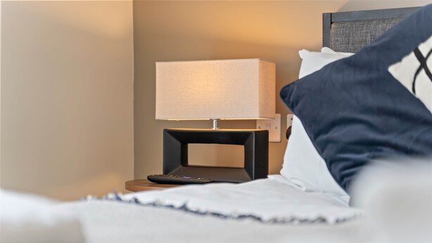 A bed with a remote control, a bedside lamp, and a pillow. - Liverpool Richmond Row 2 Bed/2 Bath Flat (107)| Secure Parking, WiFi & EV (Liverpool)