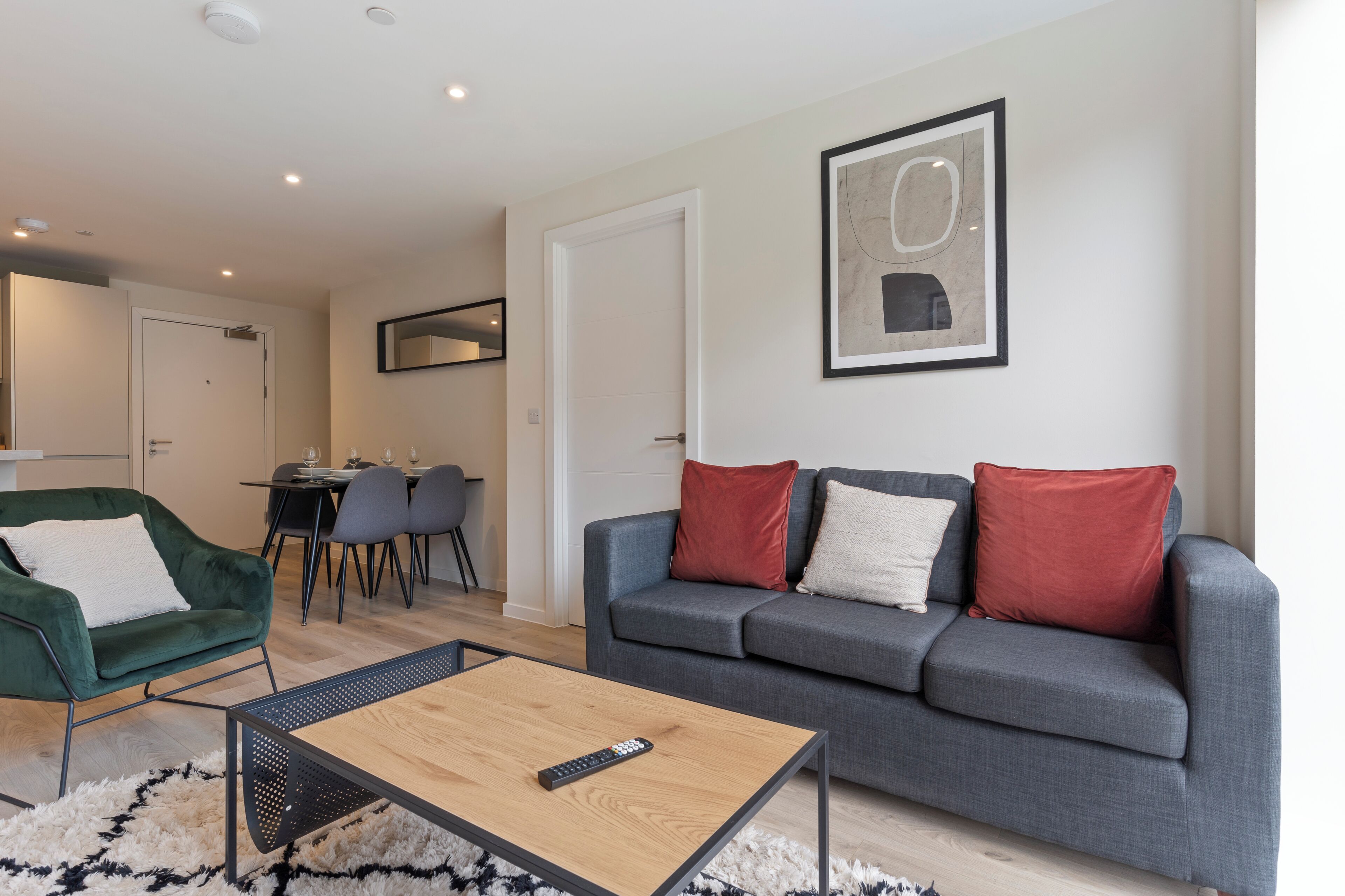 Ein Wohnzimmer mit grauem Sofa, einem grünen Sessel, einem Holztisch und einem Essbereich mit Tisch und Stühlen.