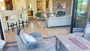 A modern living area with wicker furniture, a fireplace, and a kitchen in the background. - Stunning Villa in the Palmilla Estates. 4-bedroom house with new furniture. (La Quinta)