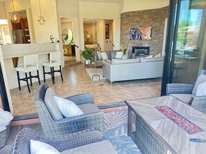 A modern living area with wicker furniture, a fireplace, and a kitchen visible in the background. - Stunning Villa in the Palmilla Estates. 4-bedroom house with new furniture. (La Quinta)