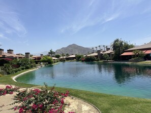 A pool with a mountain backdrop, surrounded by houses with red roofs and greenery. - Stunning Villa in the Palmilla Estates. 4-bedroom house with new furniture. (La Quinta)