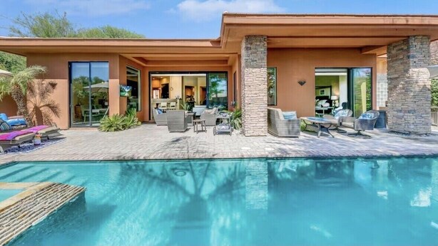 Ett modernt hus med en swimmingpool, utomhusmöbler och en stenkiosk.