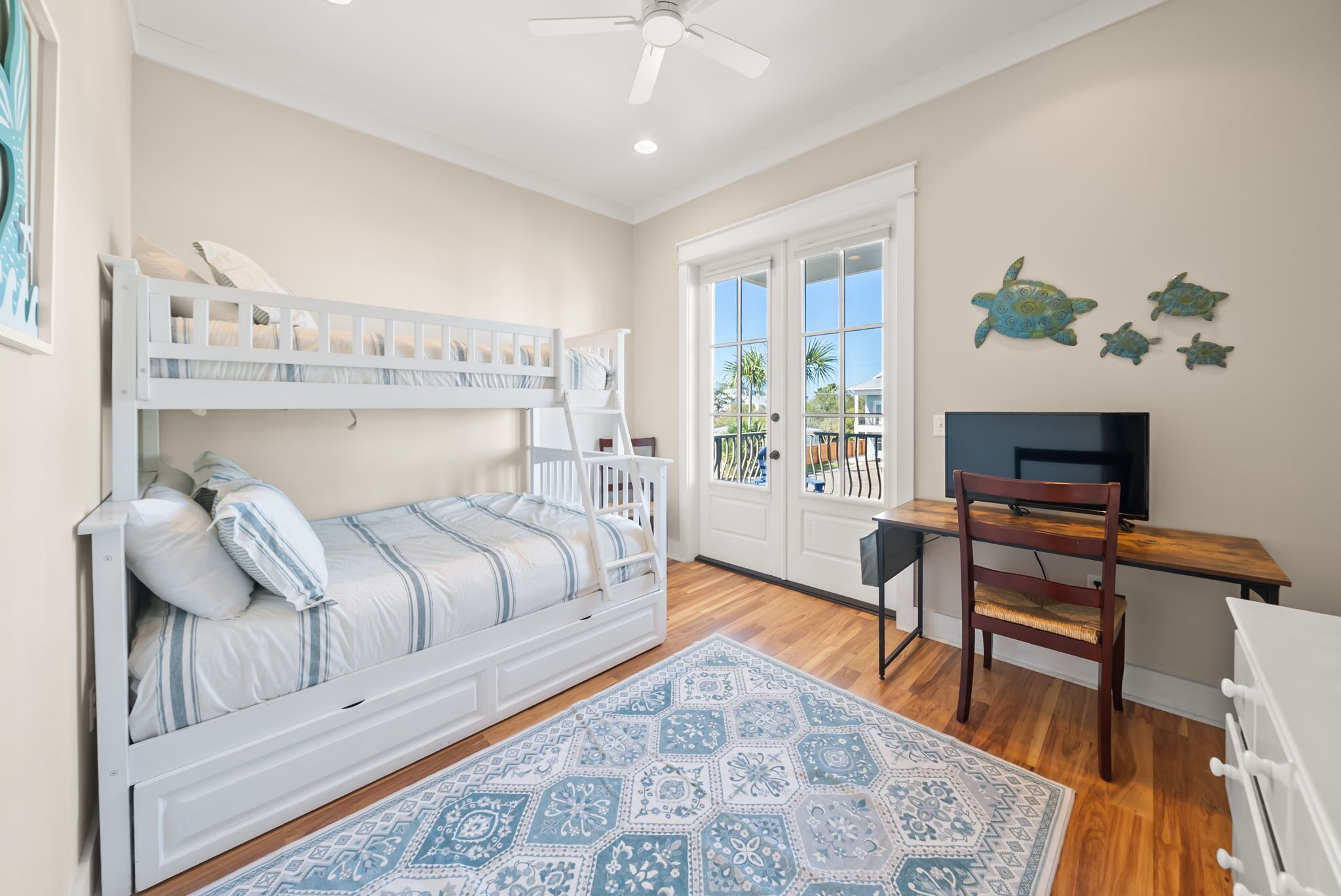 A bedroom with a bunk bed, a desk, a chair, a TV, and a patterned rug.