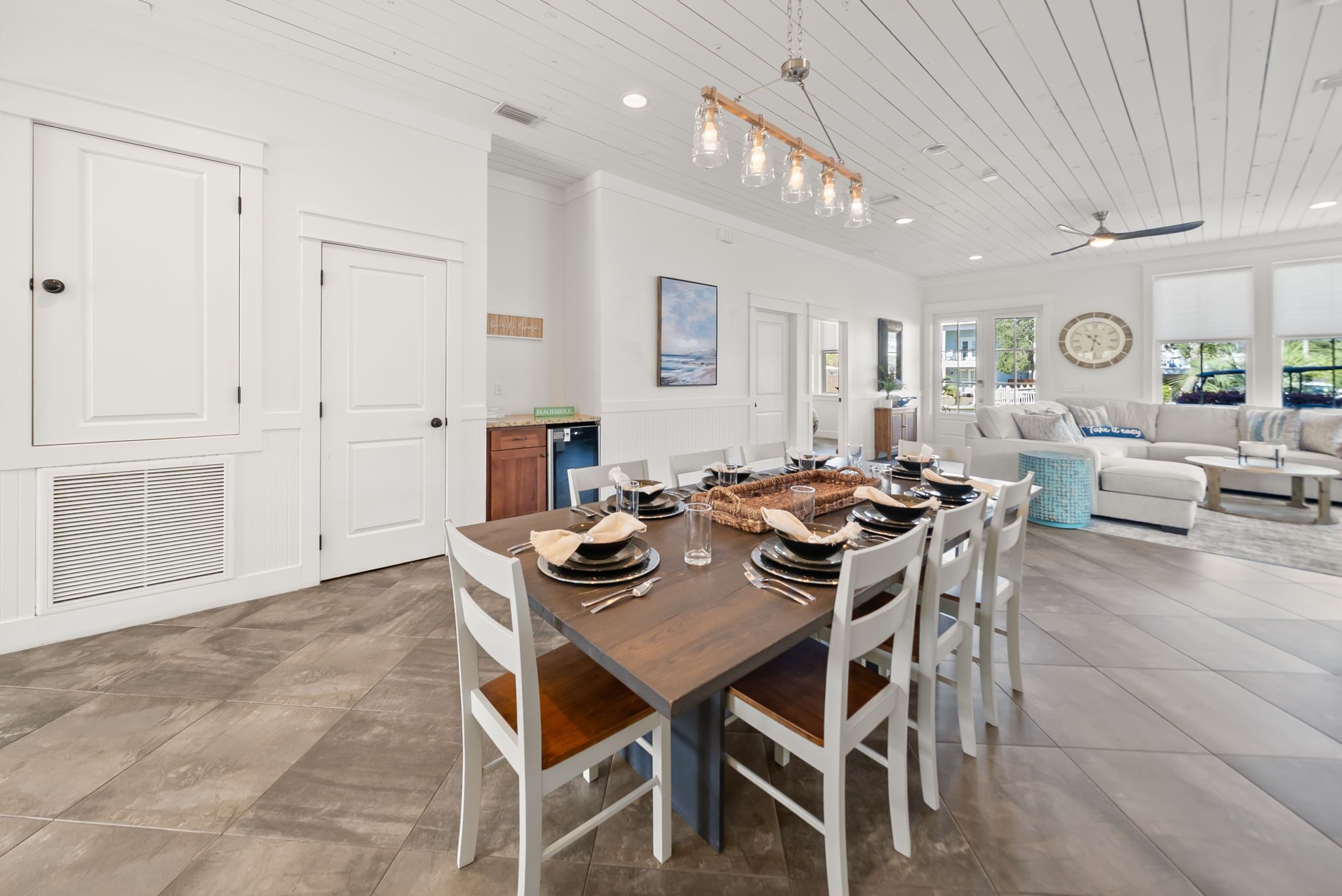 A spacious dining area with a wooden table set for six, white chairs, and a ceiling fan.