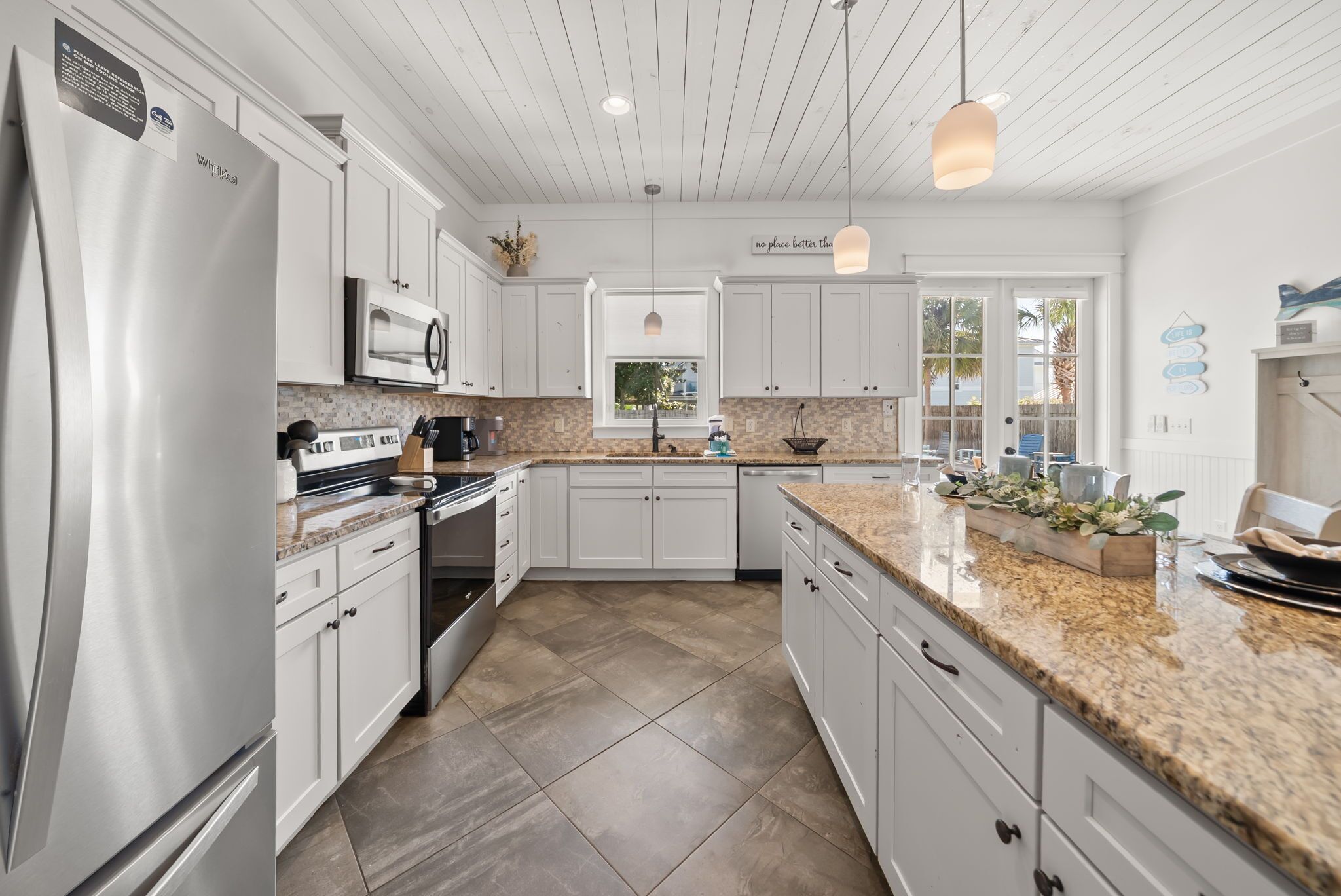 A modern kitchen with white cabinetry, granite countertops, stainless steel appliances, and a large window.