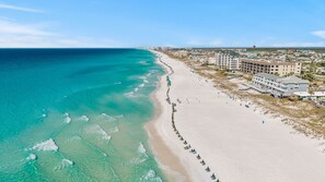 Um resort à beira-mar com uma extensa praia de areia, vista para o oceano e vários edifícios com varandas.
