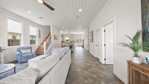 A spacious living area with a sofa, armchairs, and a coffee table. A staircase leads to a kitchen area. - Take It Easy (Destin)