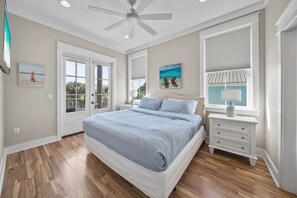 Quarto com cama, ventoinha no teto, janela com persianas, mesa de cabeceira e obras de arte nas paredes.