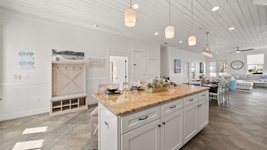 A spacious kitchen with white cabinetry, a granite countertop, pendant lighting, and a large island. - Take It Easy (Destin)