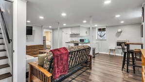 Ein modernes Wohnzimmer mit einer Couch, einer hölzernen Bank, einer Küchenzeile mit Mikrowelle und einer Treppe.