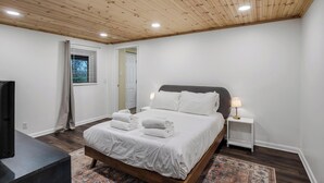 Ein Schlafzimmer mit Holzbalkendecke, einem Bett mit weißer Bettwäsche, einem Nachttisch mit Lampe und einem Fernseher auf einem Schrank.