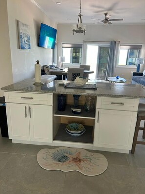 A kitchen with a central island, white cabinets, a chandelier, a flat-screen TV, and a dining area with a table and chairs. - New Oceanfront Beach House, "Paradise Blue" - Your Private Tropical Escape. (Rolleville)