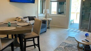A dining area with a table, chairs, and a chandelier. There is a television mounted on the wall displaying a nature scene. - New Oceanfront Beach House, "Paradise Blue" - Your Private Tropical Escape. (Rolleville)