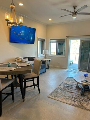 A dining area with a table, chairs, and a chandelier. There is a television mounted on the wall displaying a nature scene.