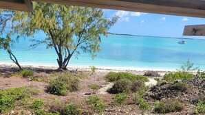 A beach view with a wooden structure, clear turquoise water, and a distant boat. - New Oceanfront Beach House, "Paradise Blue" - Your Private Tropical Escape. (Rolleville)