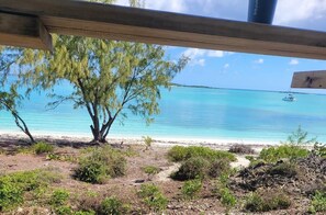 Blick auf einen Strand mit einer Holzkonstruktion, klarem türkisblauem Wasser und einem entfernten Boot.
