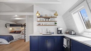 A compact bedroom with a bunk bed, a kitchenette with blue cabinets, and a window with a view. - Lone Star-New! Sleep 8 in Seal Harbor! (Mount Desert)