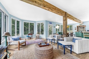 A spacious living room with large windows, a wooden ceiling beam, and a view of the outdoors. - Reef Point Cottage-Ocean views! (Bar Harbor)
