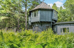 A treehouse with a stone facade and a peaked roof, surrounded by dense greenery. - Reef Point Cottage-Ocean views! (Bar Harbor)
