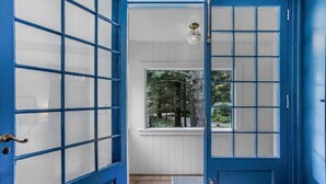 Una puerta azul con paneles de vidrio, una ventana con vistas a árboles y una lámpara sobre la puerta.