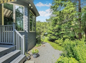 A house with a porch, a gravel path, and surrounding greenery. - Reef Point Cottage-Ocean views! (Bar Harbor)