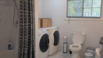 A bathroom with a walk-in shower, a toilet, a washing machine, and a window.