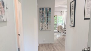 A hallway with a bench, artwork on the walls, and a view into a room with a chair.